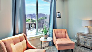 A room with a large window, a potted plant on a small table, two armchairs, and a wooden side table with a lamp. - Entrada at Moab 619 (Moab)
