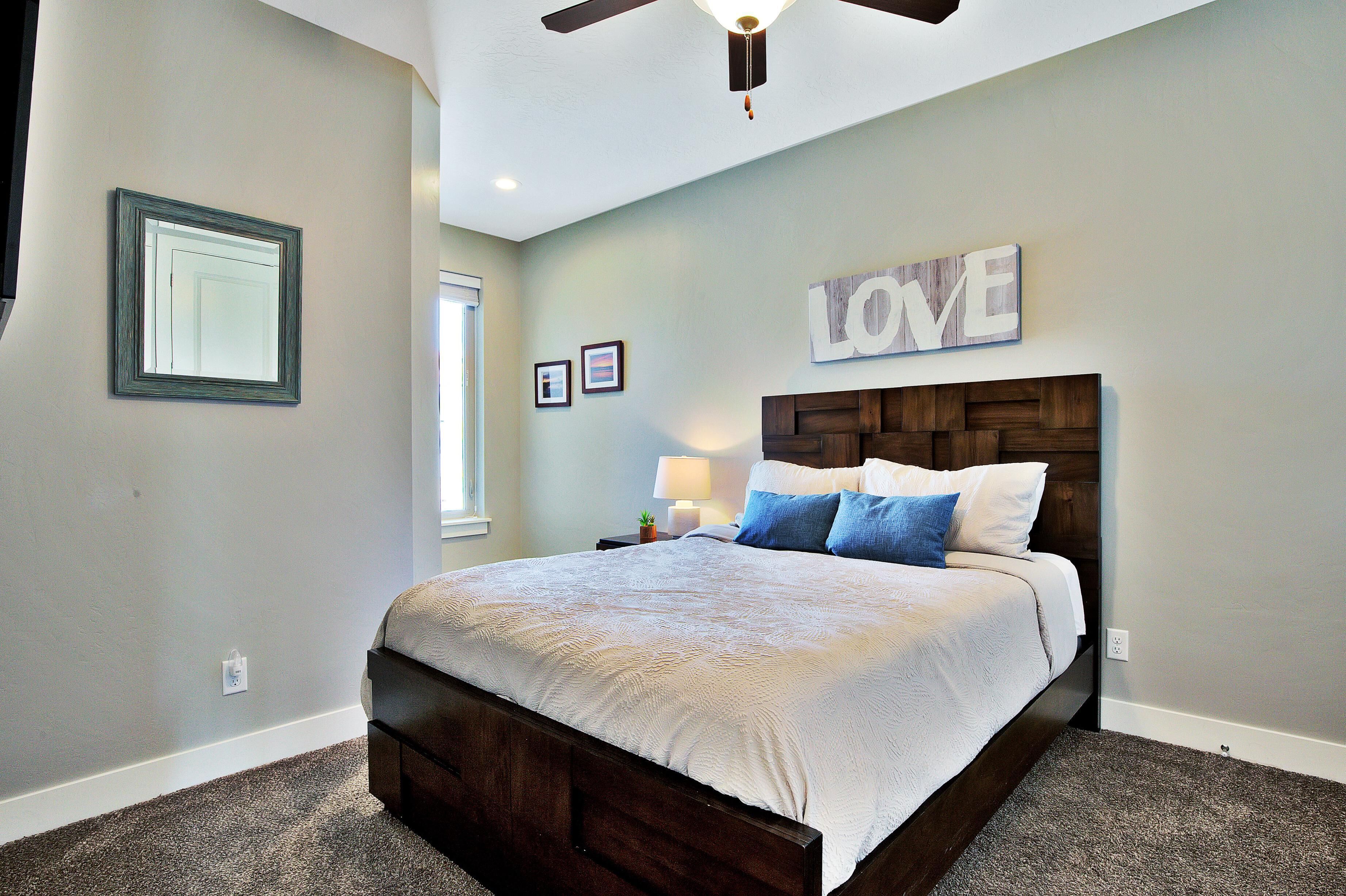 A bedroom with a bed, a ceiling fan, a wall-mounted light, and a 'LOVE' sign.