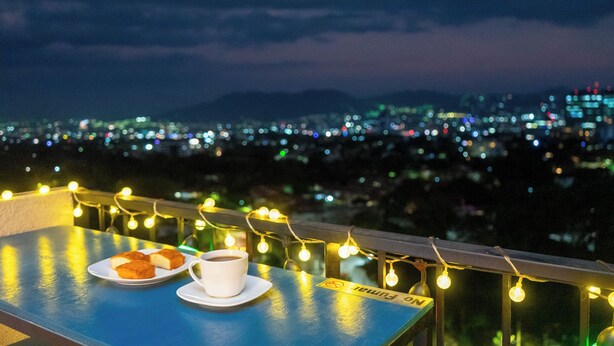 A table with pastries and a cup, string lights, and a city view at night. - Deluxe, City views, Rooftop pool, upscale location (San Salvador)