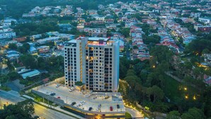 A high-rise building with multiple floors, surrounded by a residential area with houses and greenery. - Deluxe, City views, Rooftop pool, upscale location (San Salvador)