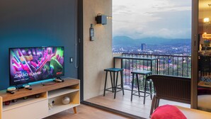 A balcony with a TV, bar stools, and a view of a cityscape. - Deluxe, City views, Rooftop pool, upscale location (San Salvador)