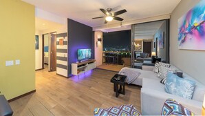 A modern living room with a flat-screen TV, a ceiling fan, and a sofa with decorative pillows. - Deluxe, City views, Rooftop pool, upscale location (San Salvador)