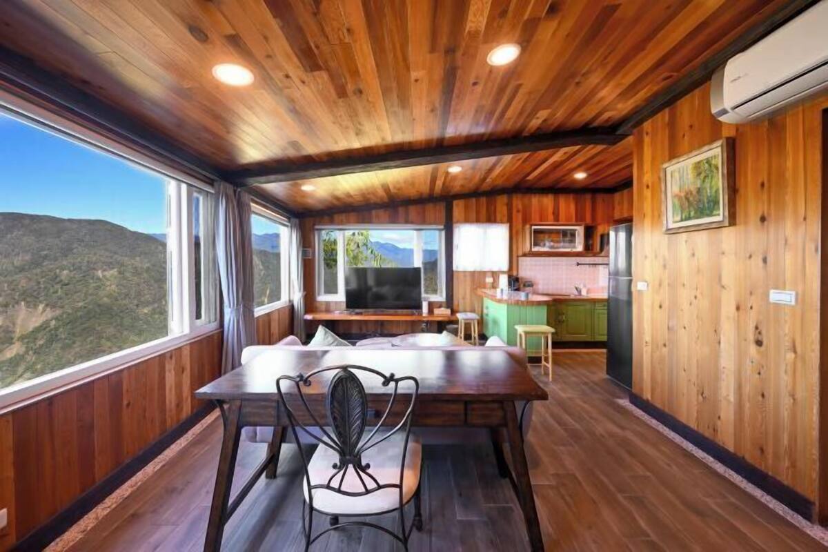 A wooden cabin with a dining area, kitchen, and large windows offering a mountain view.