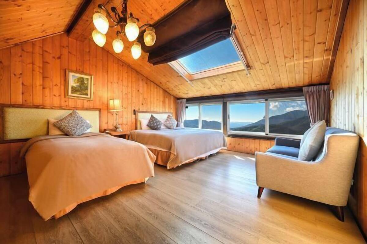 A cozy room with wooden walls, a large bed, a smaller bed, a sofa, and a skylight.