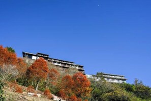 A multi-story building with a modern architectural style, situated on a hillside with autumn foliage. - Chingjing Top Cloud Resort (Nantou)