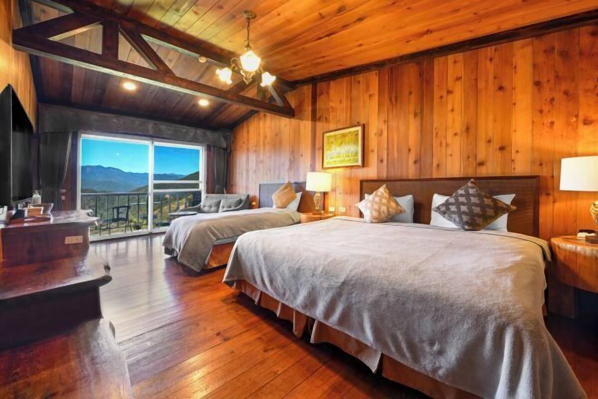 A wooden-floored bedroom with two beds, a large window, and a view of the mountains.