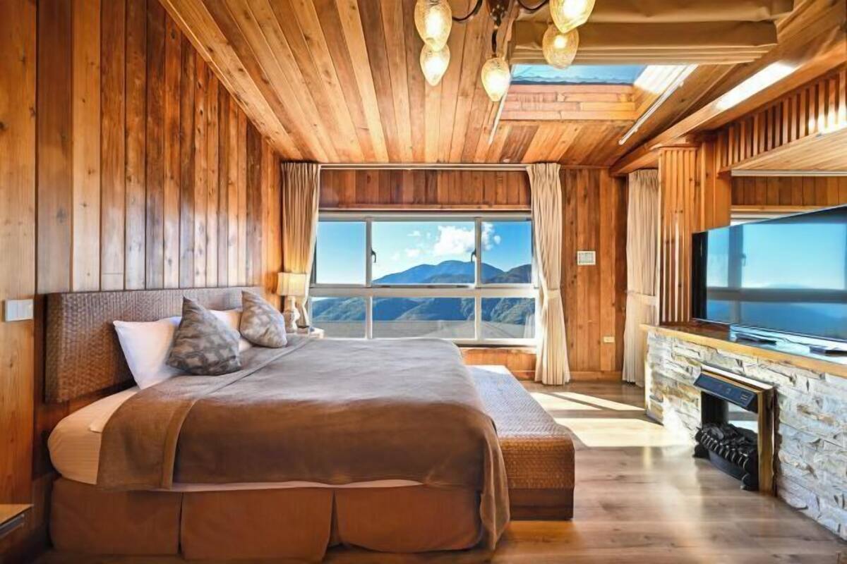 A wooden room with a large bed, a TV, and a stone fireplace.