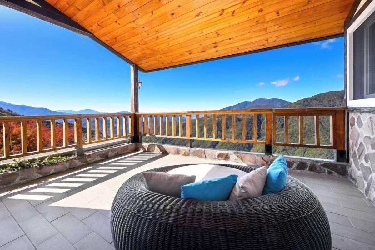 A covered balcony with a wicker sofa, stone walls, and a view of mountains.