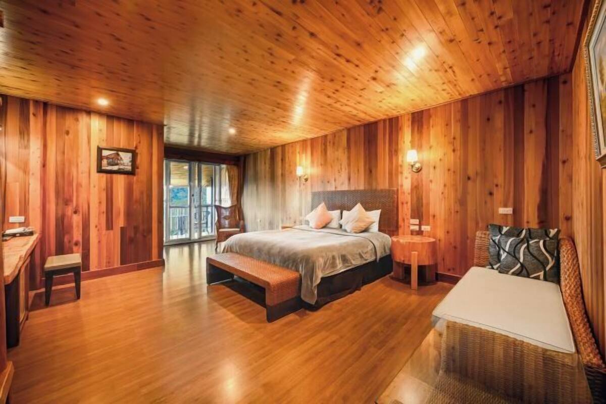 A wooden-paneled bedroom with a bed, bench, bedside table, and a view of the outdoors.