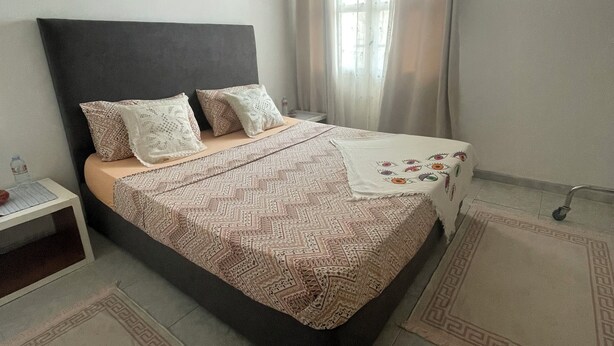 A bedroom with a bed, nightstand, and a window with curtains. - Cosy host apartment (Bir El Djir)