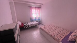 A small, sparsely furnished room with a single bed, a desk, and a window with curtains. - Cosy host apartment (Bir El Djir)