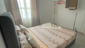 A bedroom with a bed, curtains, a hanging light, a towel rack, and a small table. - Cosy host apartment (Bir El Djir)