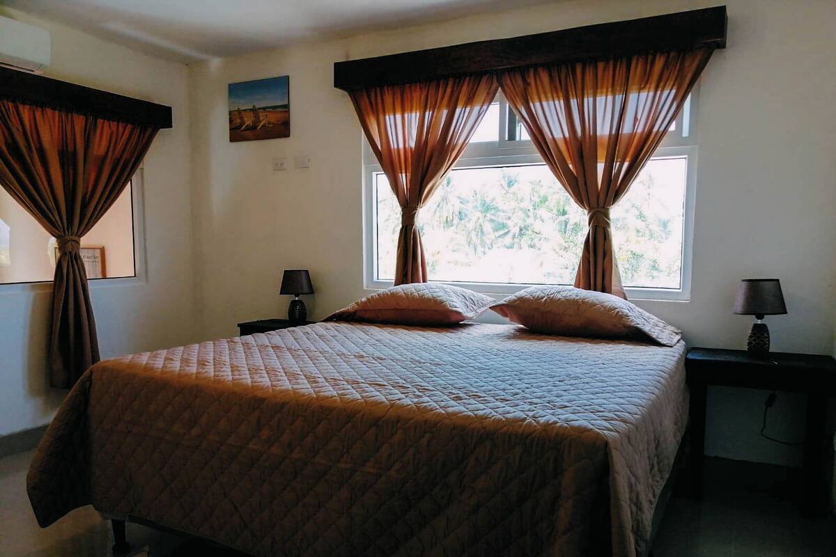Une chambre à coucher avec un grand lit, deux tables de chevet avec des lampes et des rideaux aux fenêtres.