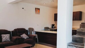 Een moderne woonkamer met een donkerbruine zithoek, een houten salontafel, en een keuken met een gasfornuis en kastjes.