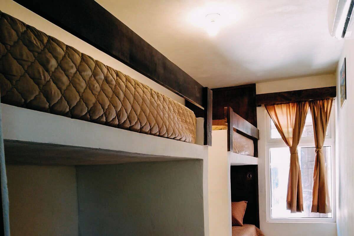 Une chambre avec des lits superposés, une fenêtre avec des rideaux et un sol carrelé.