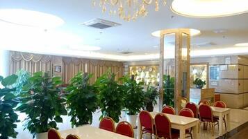 Un espace de restauration d’hôtel avec des tables rondes, des chaises rouges et des plantes en pot.