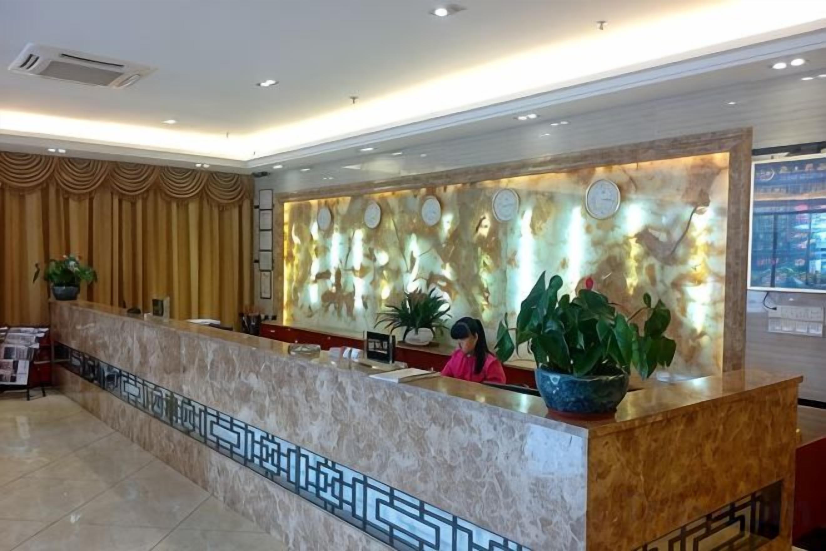 A hotel reception area with a marble counter, decorative wall, and potted plants.