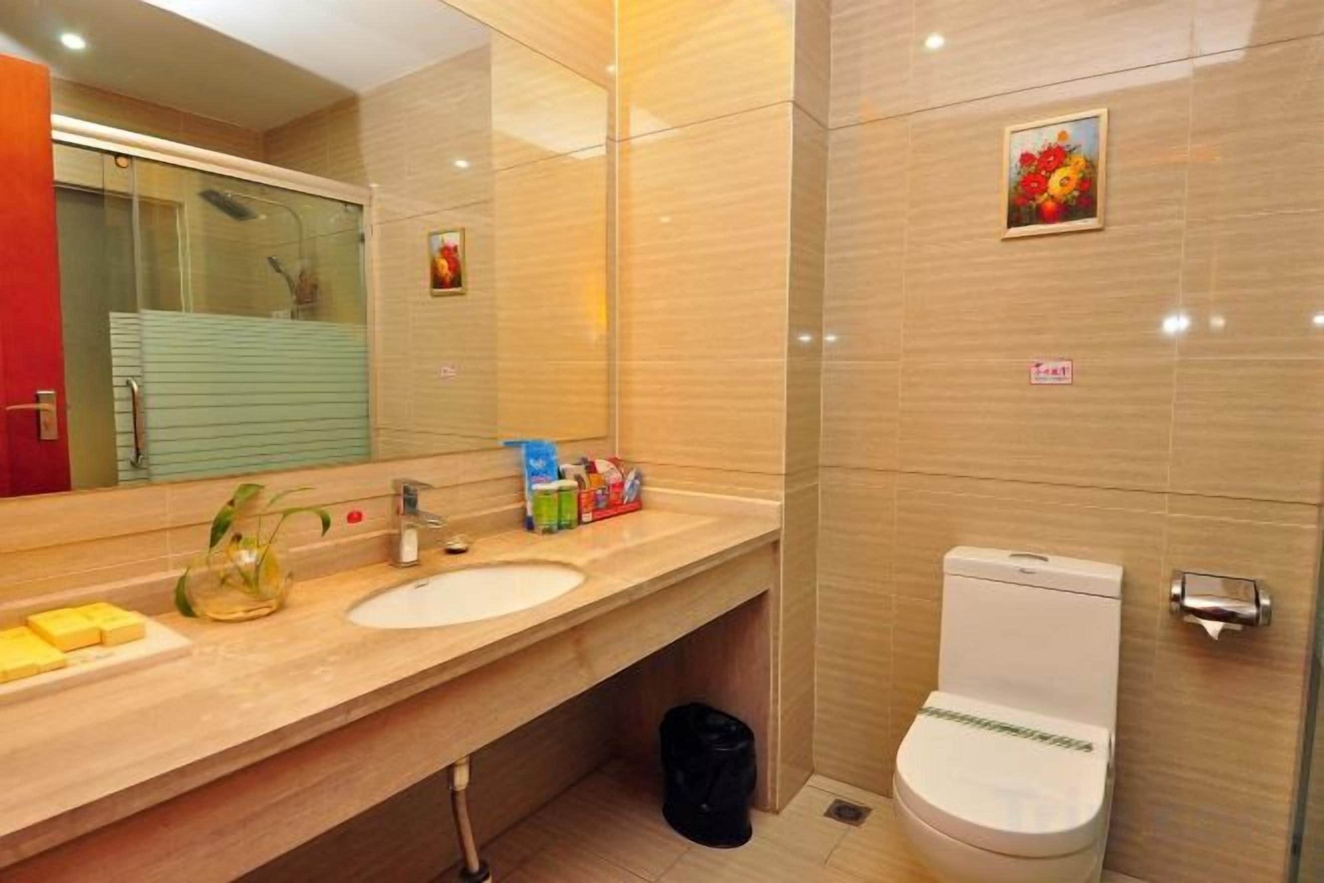 Une salle de bain avec un double lavabo, des toilettes, un miroir et une poubelle.