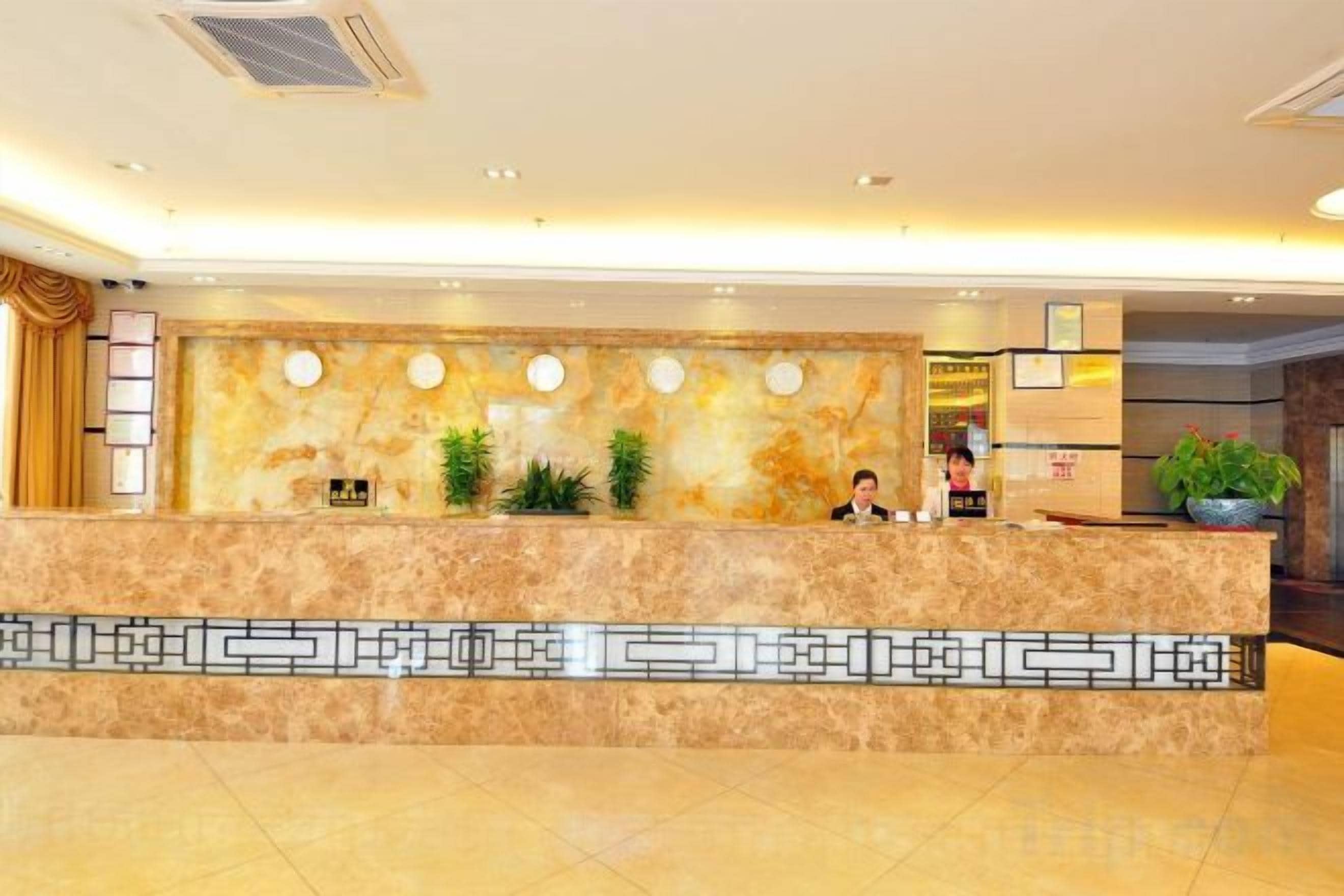 Een hotel receptie met een marmeren balie, planten en een modern plafondontwerp.