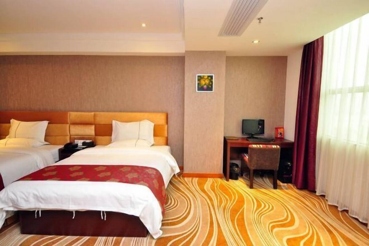 Quarto de hotel com duas camas, uma escrivaninha, televisão e uma janela grande com cortinas.