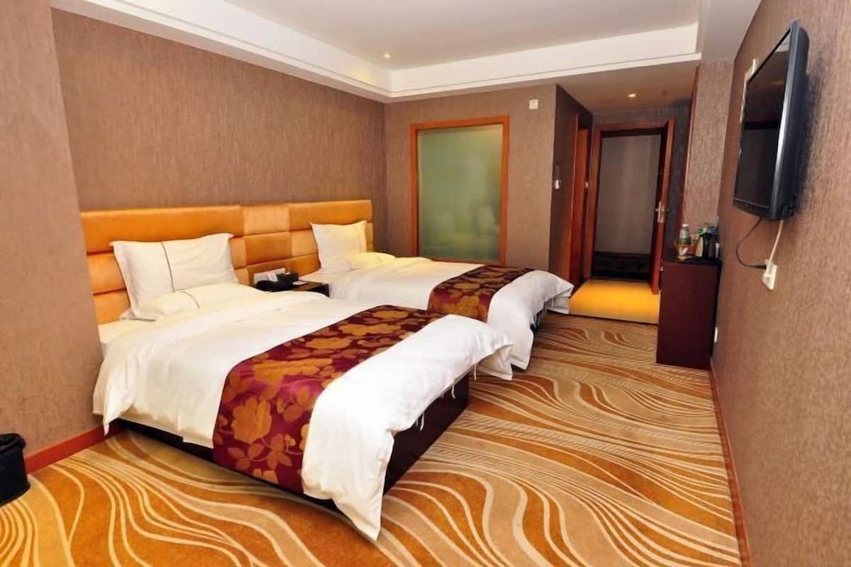 Quarto de hotel com duas camas, uma televisão e piso coberto por carpete.