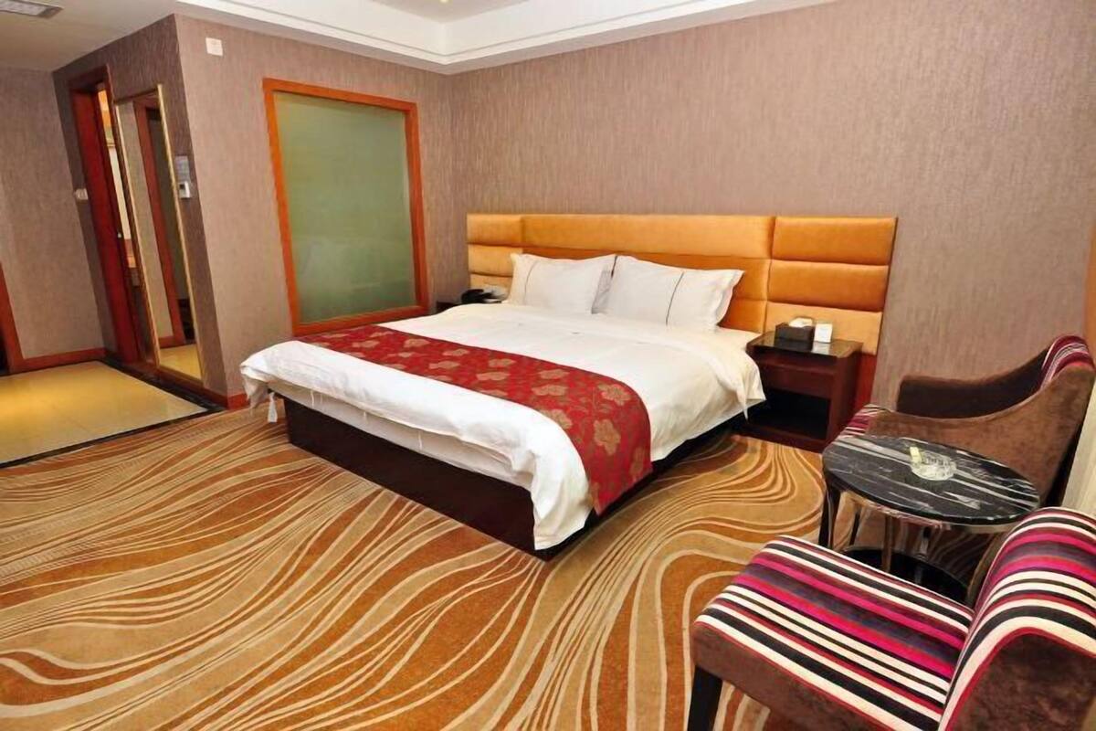 Quarto de hotel com uma cama grande, uma mesa de cabeceira, uma cadeira e uma pequena mesa.