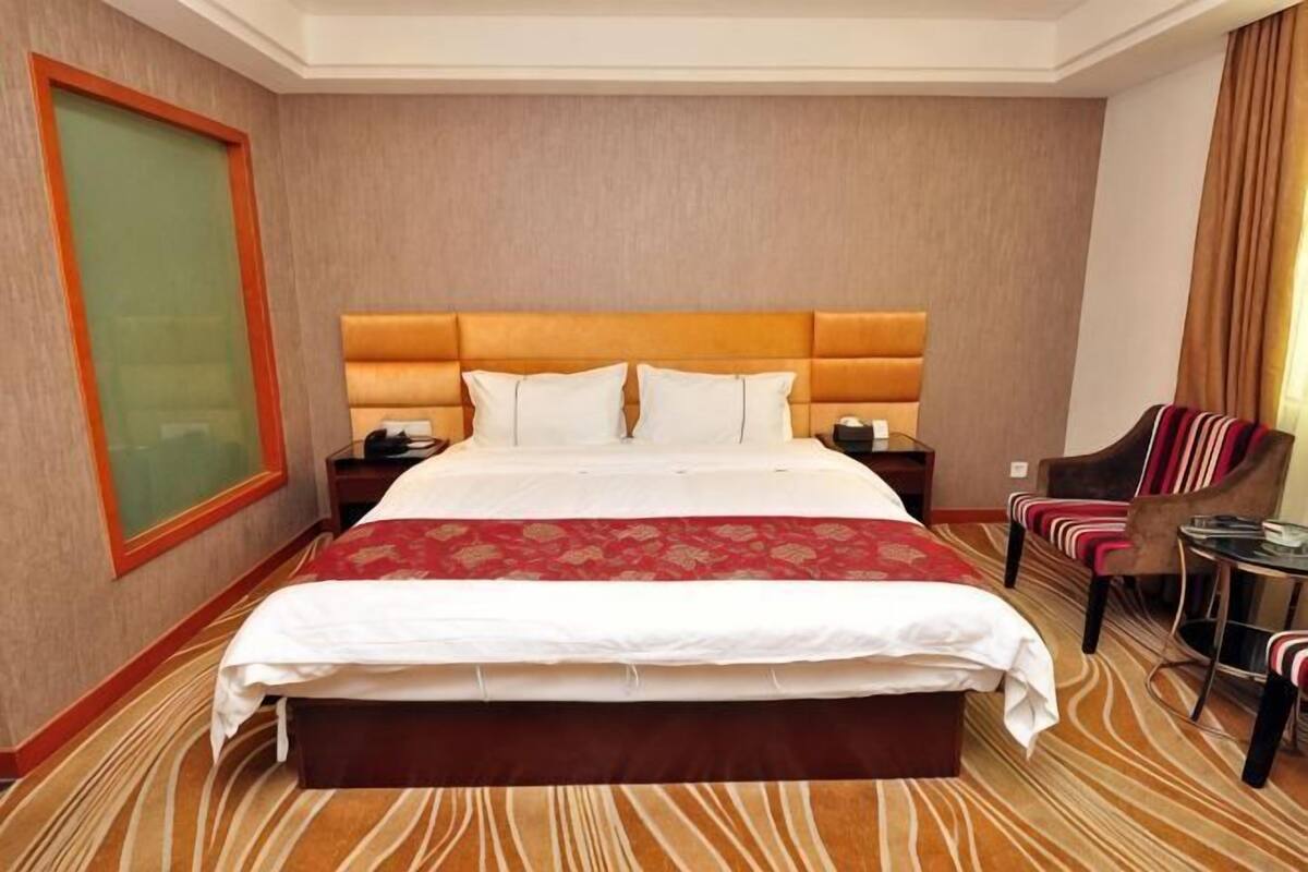 Quarto de hotel com uma cama grande, cabeceira, mesa de cabeceira, uma cadeira e vista para o exterior.