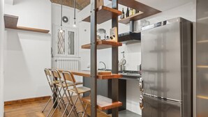 A compact kitchen with a built-in refrigerator, wooden stools, and a mezzanine shelf with kitchenware. - Pretorius Design Loft - Near Termini Station by RHR (ROMA)