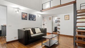 A modern living room with a black leather sofa, a glass coffee table, wooden flooring, and a loft-style staircase. - Pretorius Design Loft - Near Termini Station by RHR (ROMA)