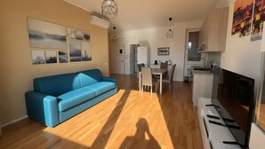 A modern living room with a blue sofa, wooden flooring, a dining area with a table and chairs, and a kitchen with a TV and appliances. - Modern Apartment near Tiburtina Station by RHR (ROMA)