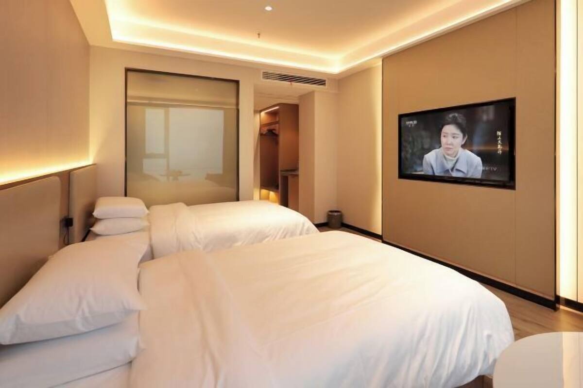 Habitación de hotel con dos camas, un televisor en la pared y un ventanal grande.