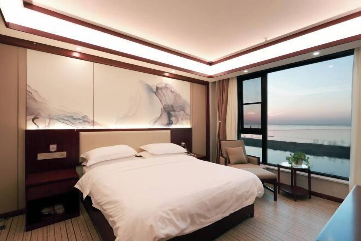 Una habitación de hotel con una cama grande, una silla, una mesita y vista al agua.