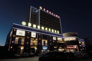 A multi-story hotel with illuminated signage and a parking lot in front.