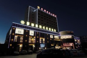 A hotel with multiple floors, illuminated signage, and a parking lot in front. - Huoqiudu International Hotel (Huoqiu)
