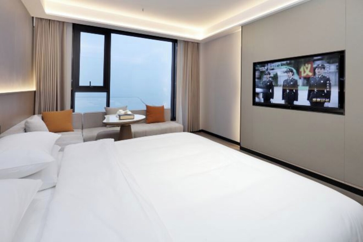 Habitación de hotel con una cama grande, un sofá, una mesita y un televisor en la pared.