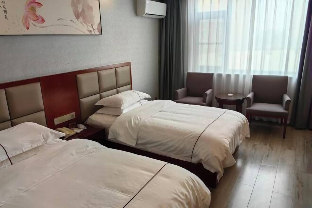 Habitación de hotel con dos camas, una mesita, una silla y un cuadro en la pared.