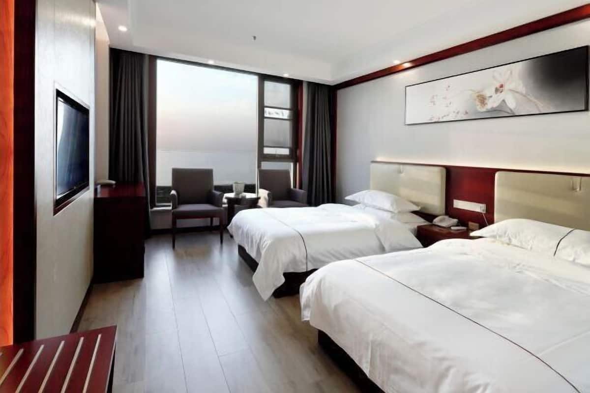 Habitación de hotel con dos camas, un escritorio, una silla, un televisor y un amplio ventanal.