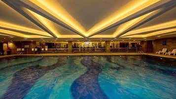 Una amplia piscina interior con una zona central de observación, rodeada de asientos y un diseño de techo moderno.