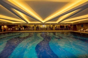 Una amplia piscina interior con una zona central de observación, rodeada de asientos y un diseño de techo moderno.