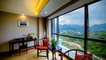 Una habitación con un ventanal grande, un escritorio, dos sillas y una mesita con una planta.