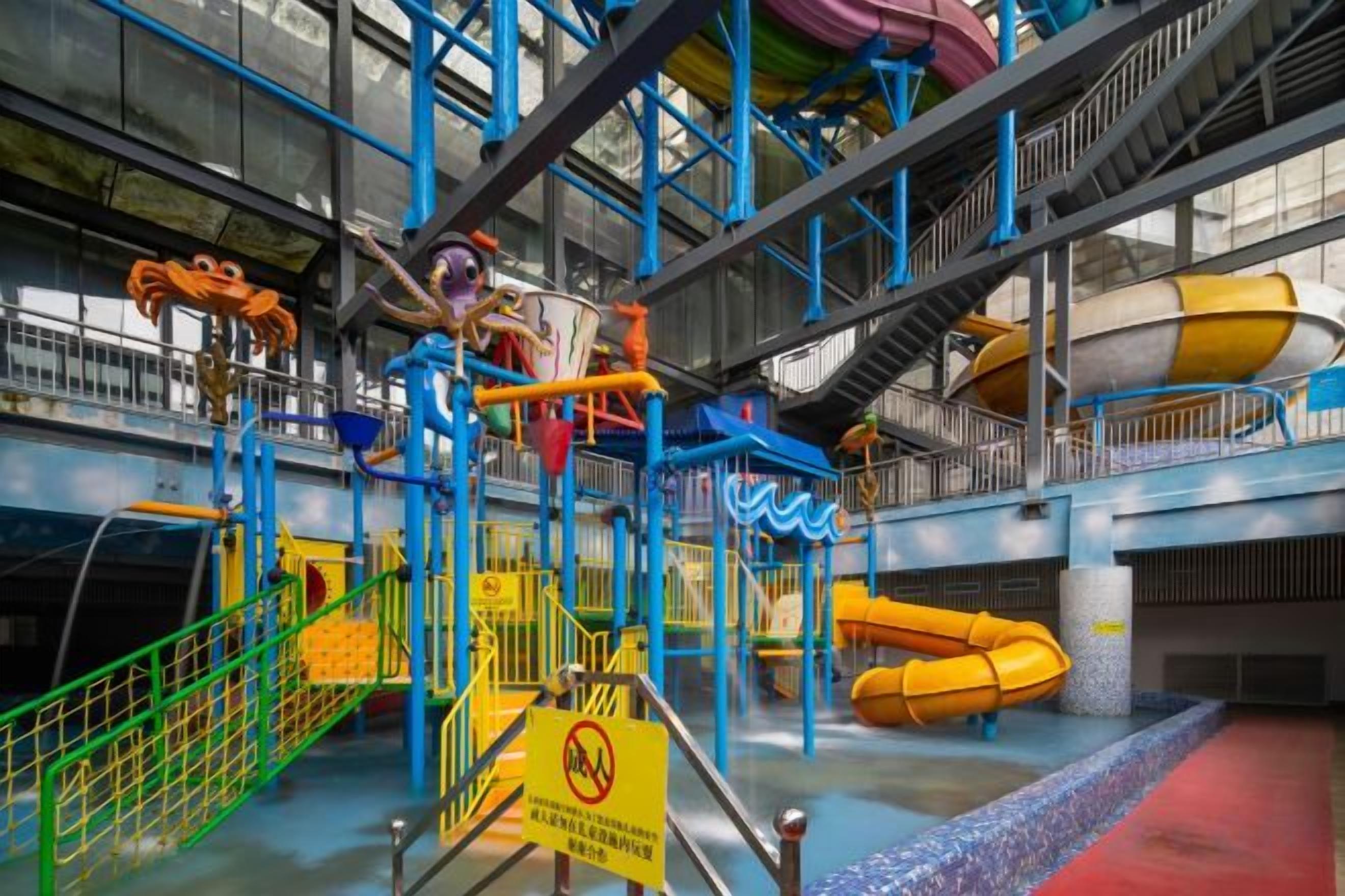 Parque acuático interior con toboganes y un letrero de precaución.