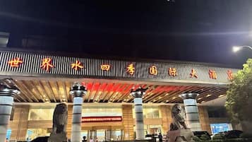 Entrada de un hotel con un gran letrero en caracteres chinos, dos estatuas de leones y un diseño arquitectónico moderno.