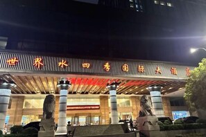 Entrada de un hotel con un gran letrero en caracteres chinos, dos estatuas de leones y un diseño arquitectónico moderno.