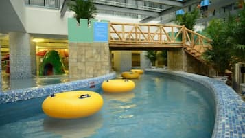 Una piscina interior con anillos flotantes amarillos, un puente y una planta tropical.