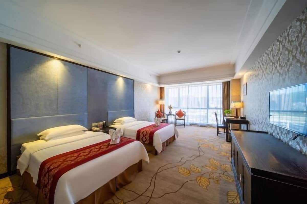Ein Hotelzimmer mit zwei Betten, einem Schreibtisch, einem Stuhl, einem Fernseher und einem großen Fenster mit Blick.