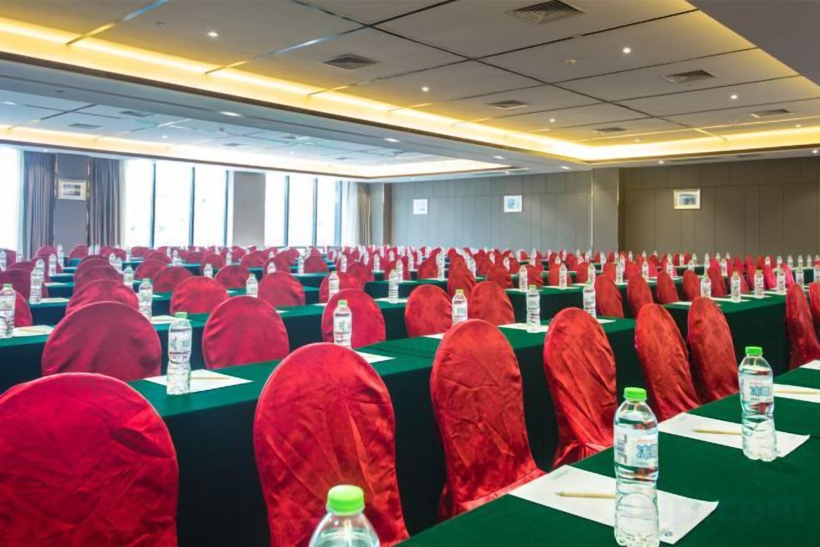 Un salón de conferencias con filas de mesas, cada una con una funda roja para la silla, botellas de agua y documentos.