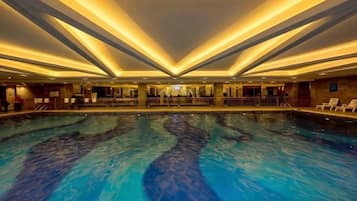 Una gran piscina coberta amb una zona central d'observació, envoltada de seients relaxants i un sostre elevat amb il·luminació lineal.