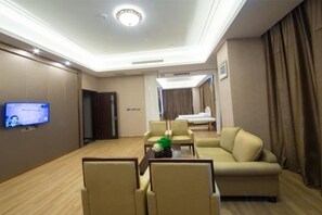 A hotel room with a flat-screen TV, a sofa, a coffee table, and a bed.