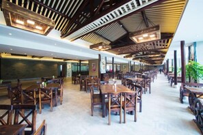 Un restaurant spacieux avec de hauts plafonds et des poutres en bois, doté de nombreuses tables et chaises disposées pour accueillir les clients.