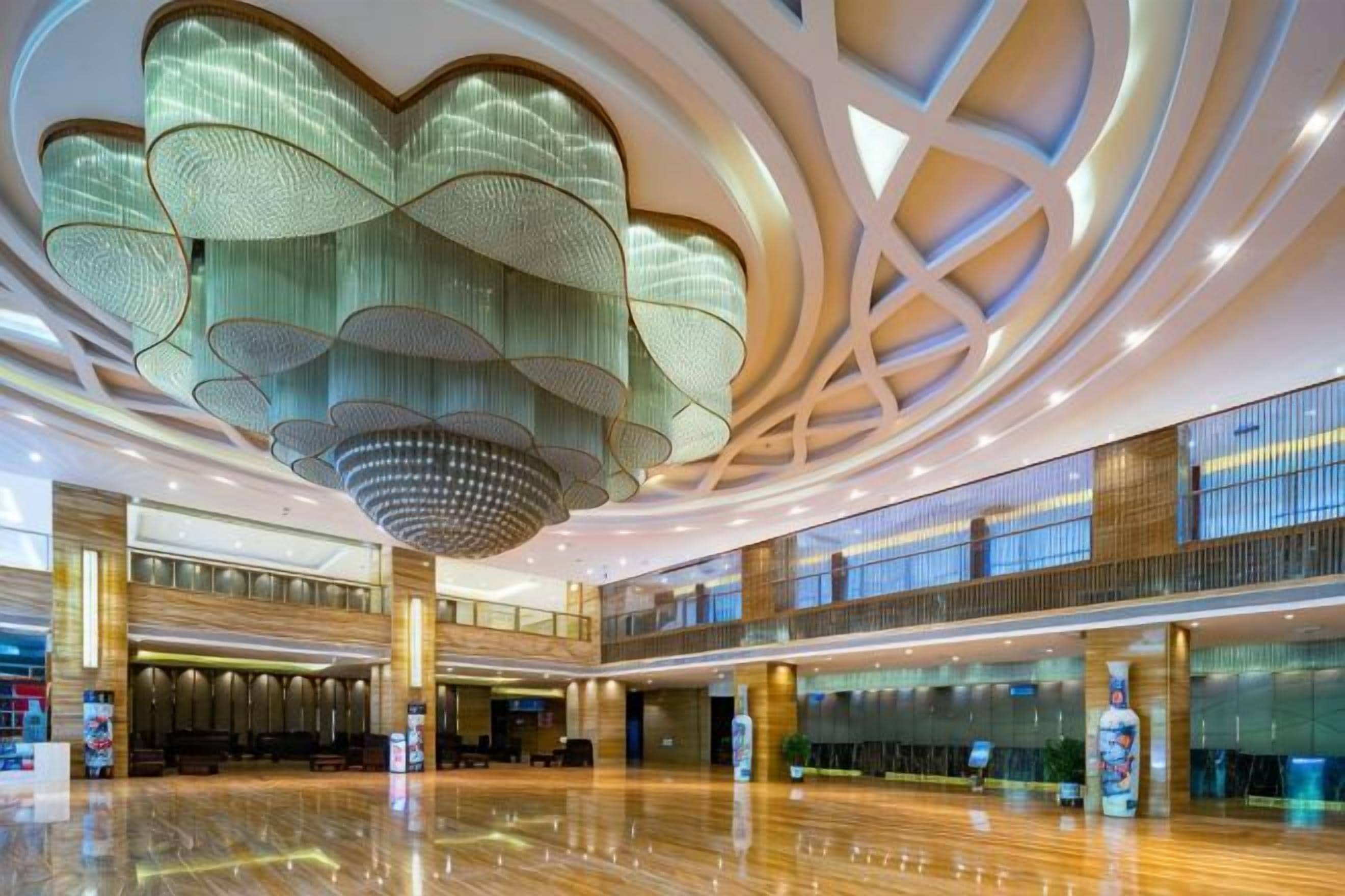 A spacious lobby with a large, modern chandelier and a polished wooden floor.
